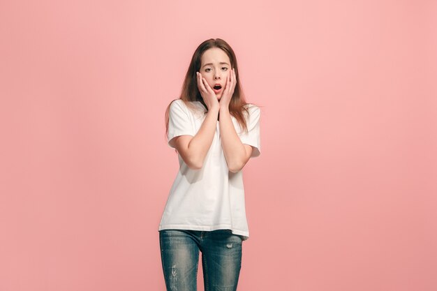 Schönes jugendlich Mädchen, das überrascht auf rosa Wand sucht