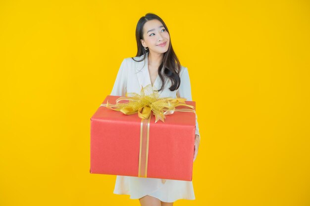 Schönes junges asiatisches Frauenlächeln des Porträts mit roter Geschenkbox auf Farbhintergrund