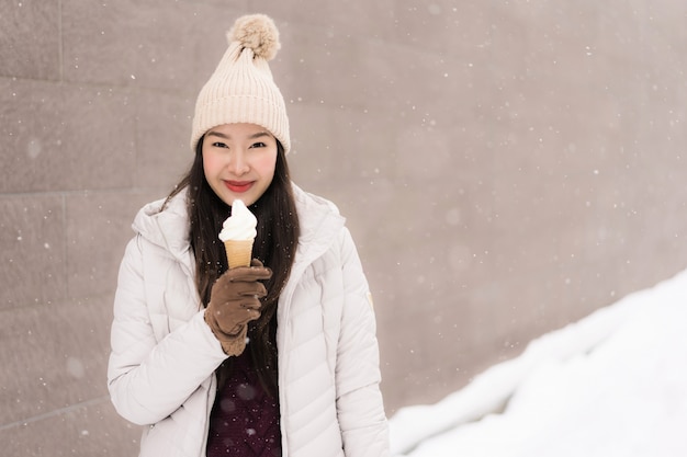 Schönes junges asiatisches frauenlächeln und glücklich mit eiscreme in der schneewintersaison