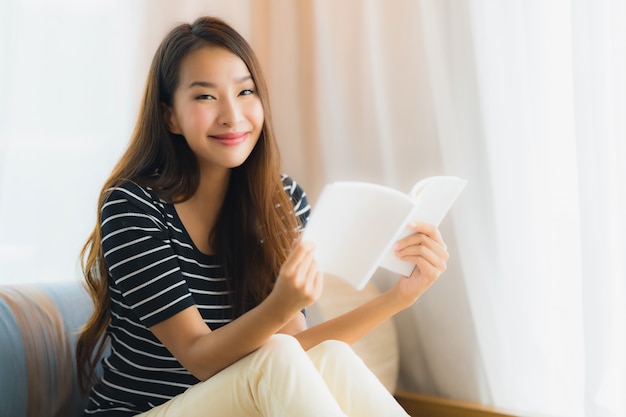 Schönes junges asiatisches Frauenlesebuch des Porträts herein auf Sofa im Wohnzimmerbereich