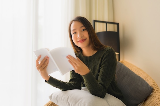 Schönes junges asiatisches Frauenlesebuch des Porträts und Sitzen auf Sofastuhl