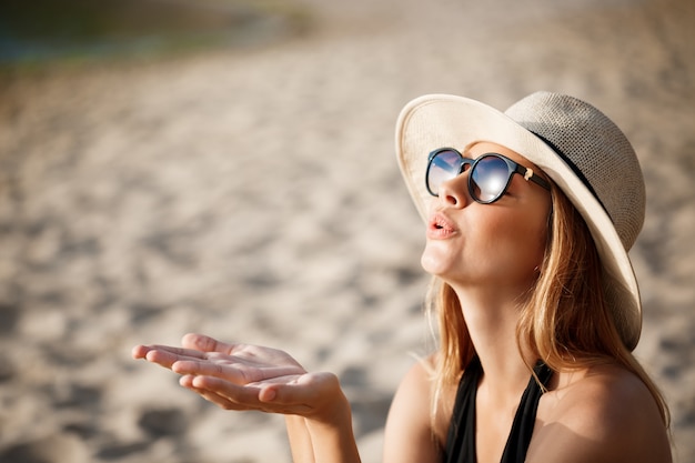 Kostenloses Foto schönes junges fröhliches mädchen, das brille und hut trägt, ruht am morgenstrand