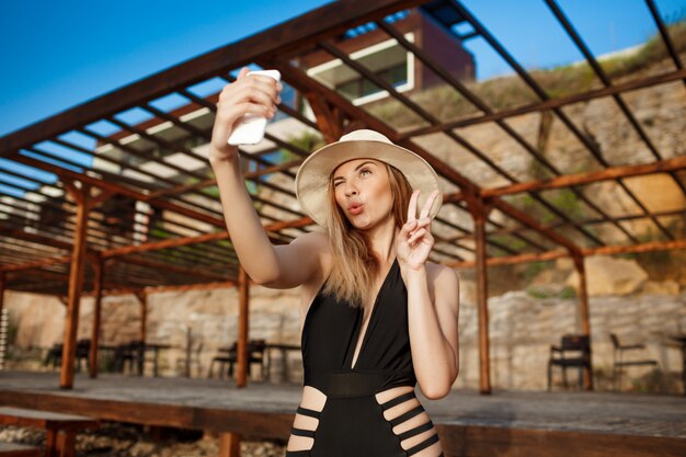 Schönes junges fröhliches Mädchen ruht am Morgenstrand, der selfie macht