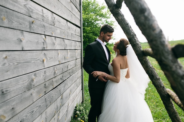 Schönes junges Hochzeitspaar steht nahe dem alten Holzhaus