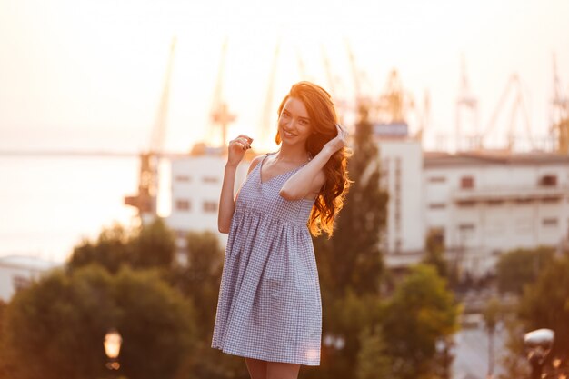 Schönes junges Ingwermädchen im Kleid, das auf dem Sonnenuntergang aufwirft