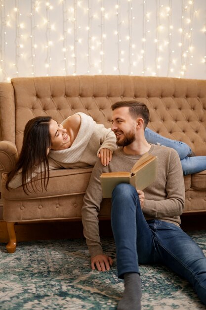 Schönes junges liebendes Paar, das aneinander bindet und lächelt, während Frau ein Buch hält.