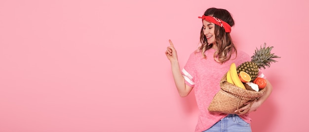 Schönes junges Mädchen im rosa T-Shirt, hält einen vollen Strohsack der Frucht auf rosa Hintergrund