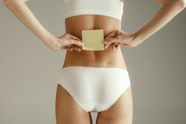 Schönes junges Modell. Nackter Rücken einer Frau, lokalisiert auf grauem Hintergrund. Hautpflege-Behandlungskonzept. Schöner weiblicher Körper