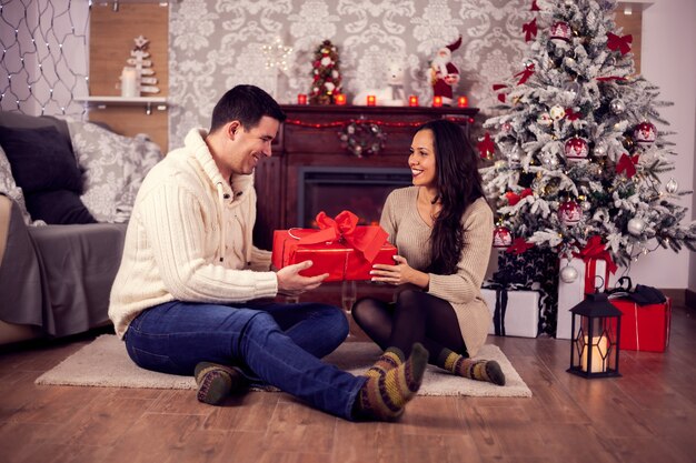 Schönes junges Paar, das sich auf den Boden setzt und Weihnachten feiert. Weihnachtsbaum. Weihnachtsgeschenkbox.