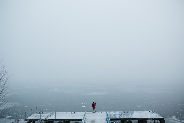 Schönes junges Paar steht auf einem Pier und schaut auf den zugefrorenen See