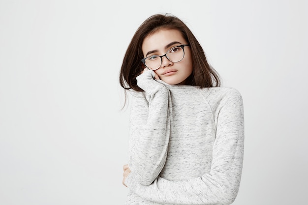 Schönes junges weibliches Modell mit dunklem glattem Haar, langärmeligem T-Shirt und Brille tragend