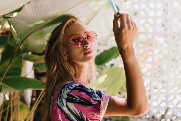 Schönes kaukasisches Mädchen in der rosa Sonnenbrille, die grüne Pflanze berührt.