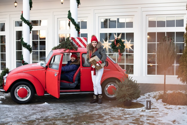 Schönes kaukasisches Mädchen in der warmen Winterkleidung trägt Kisten mit Weihnachtsgeschenken in einem roten Auto zu ihrem Ehemann