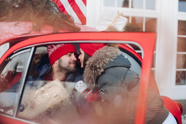 Schönes kaukasisches Mädchen in der warmen Winterkleidung trägt Kisten mit Weihnachtsgeschenken in einem roten Auto zu ihrem Ehemann