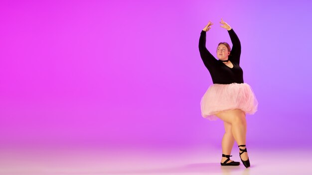 Schönes kaukasisches Plusgrößenmodell, das Balletttanz auf lila-rosa Studiohintergrund des Gradienten im Neonlicht übt. Konzept von Motivation, Inklusion, Träumen und Erfolgen. Es lohnt sich, Ballerina zu sein.