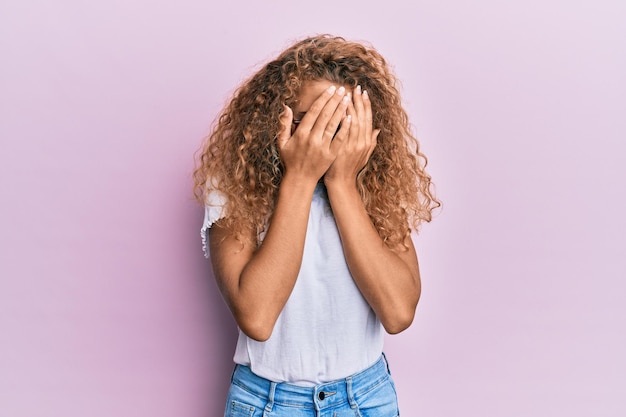 Kostenloses Foto schönes kaukasisches teenager-mädchen trägt weißes t-shirt auf rosa hintergrund mit traurigem gesichtsausdruck, das gesicht mit den händen bedeckt, während es weint depressionskonzept