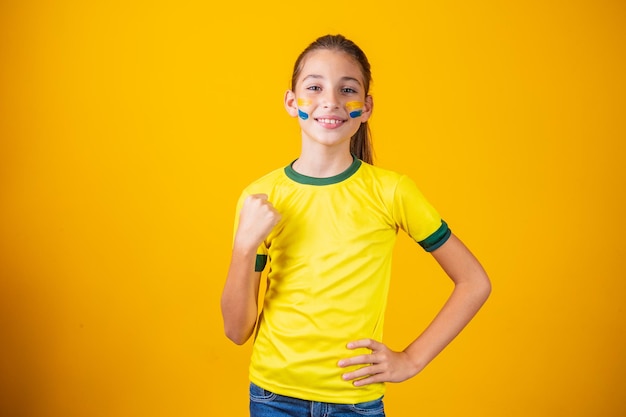 Schönes kleines mädchen, das für ihr team auf gelbem hintergrund wurzelt. kleines mädchen feiert das tor und feiert brasiliens sieg