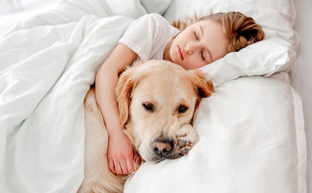 Schönes kleines mädchen, das mit golden retriever hund im bett