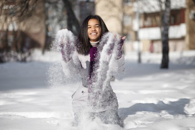 Schönes lächelndes amerikanisches Mädchen, das im Schnee draußen spielt mit Schnee sitzt