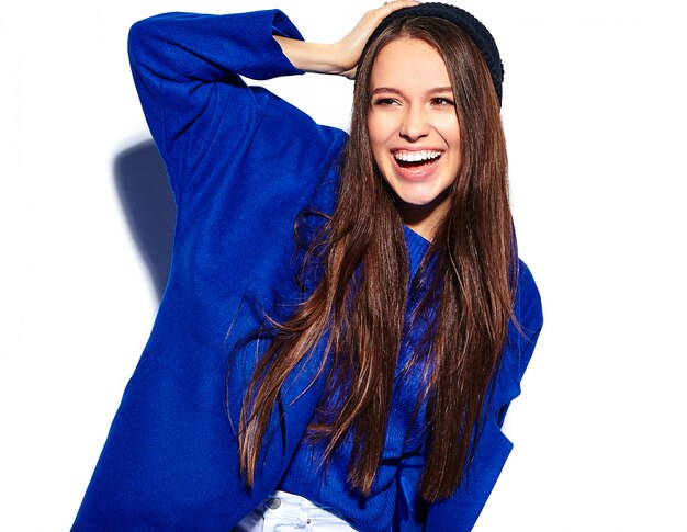 Schönes lächelndes Hipster-Brünettenfrauenmodell im stilvollen blauen Mantel lokalisiert auf Weiß
