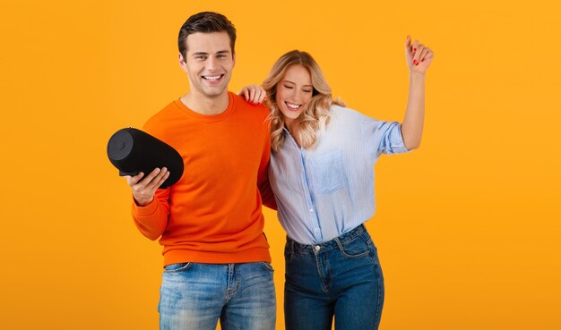 Schönes lächelndes junges Paar, das drahtlosen Lautsprecher hält, der Musik hört, die emotionale bunte Artglücksstimmung auf gelbem Hintergrund tanzt