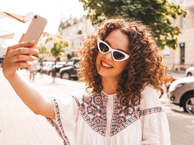 Schönes lächelndes Modell mit Afrolockenfrisur kleidete im weißen Kleid des Sommerhippies an.