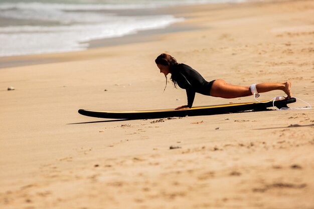 Schönes Mädchen auf einem Surfbrett auf dem Sand aufstehen.