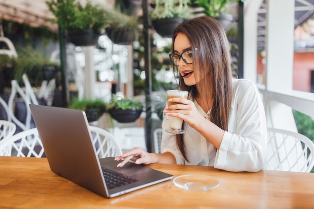 Schönes Mädchen, das am Sommertag Latte im Café trinkt