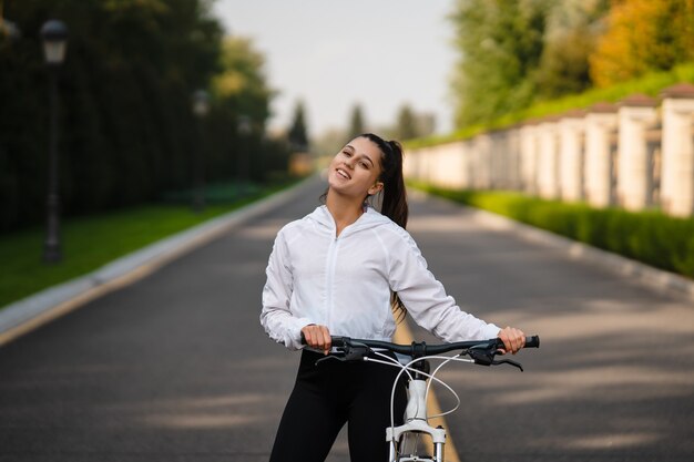 Schönes Mädchen, das am weißen Fahrrad aufwirft. Spazieren Sie in der Natur.