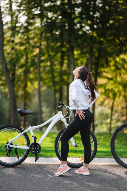 Schönes Mädchen, das am weißen Fahrrad aufwirft. Spaziergang in der Natur. Gesunder Lebensstil.