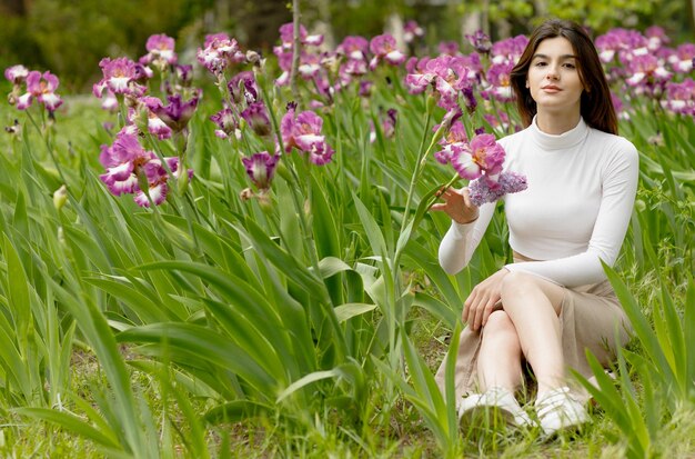 Schönes Mädchen, das auf dem Boden im Garten sitzt und eine berührende Blume mit den Händen genießt