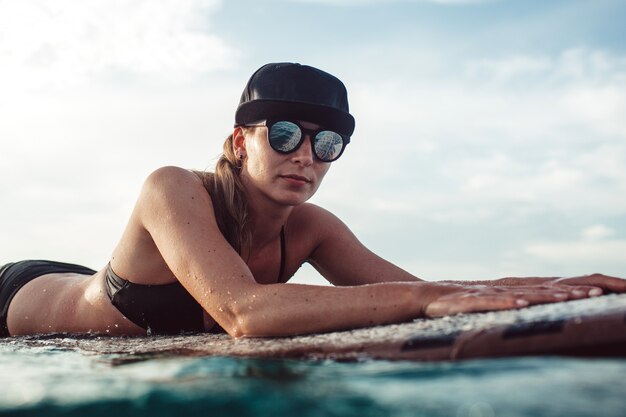 Schönes Mädchen, das das Sitzen auf einem Surfbrett im Ozean aufwirft