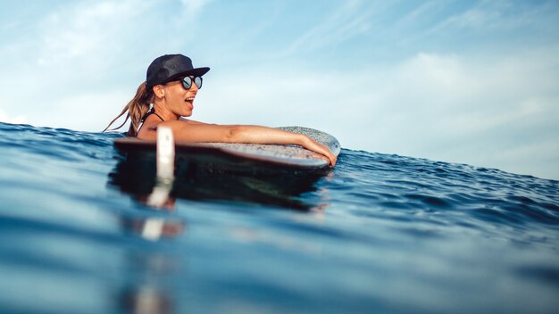 Schönes Mädchen, das das Sitzen auf einem Surfbrett im Ozean aufwirft