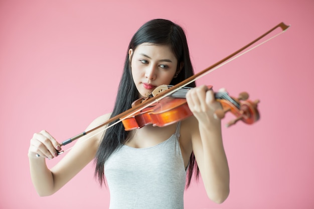 schönes Mädchen, das die Violine auf rosa Hintergrund spielt