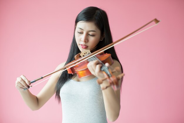 schönes Mädchen, das die Violine auf rosa Hintergrund spielt