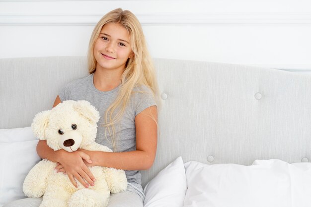 Schönes Mädchen, das im Bett mit ihrem Teddybären sitzt