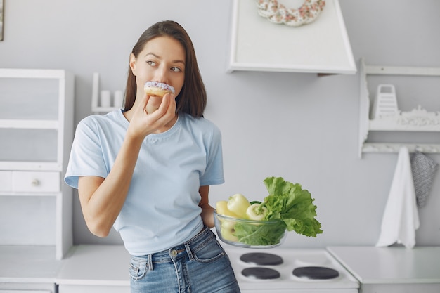 Schönes Mädchen, das in einer Küche mit Donut steht