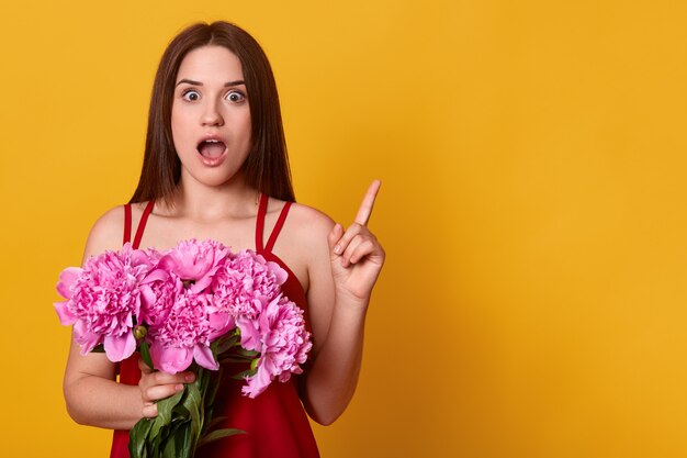 Schönes Mädchen, das mit Blumenstrauß der rosigen Pfingstrosen in ihren Händen steht