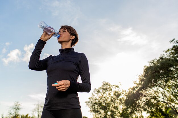 Schönes Mädchen, das Wasser von einer Flasche im Park trinkt.