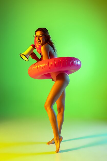 Schönes Mädchen im modischen Badeanzug einzeln auf Farbverlaufsstudio im Neonlicht.
