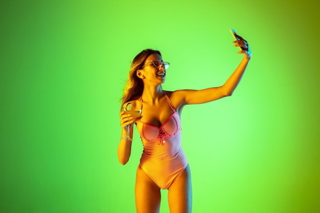 Schönes mädchen im modischen badeanzug einzeln auf gradientenstudiohintergrund im neonlicht