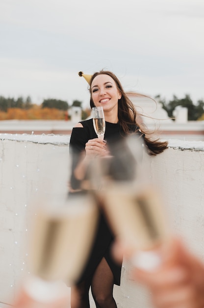 Schönes Mädchen im schwarzen Kleid auf dem Hintergrund des Aufmunterns von Champagnergläsern
