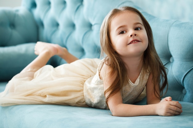 Schönes Mädchen in beige Kleid liegt auf blauem Sofa