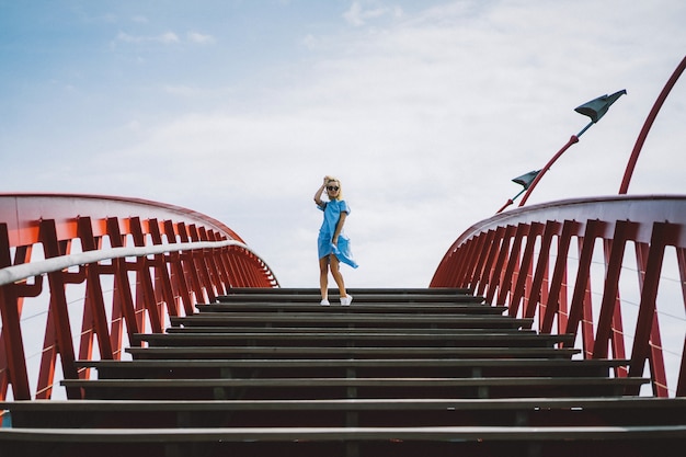 schönes Mädchen in einem blauen Kleid posiert auf der Brücke