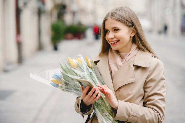 Schönes Mädchen in einem braunen Mantel. Frau in einer Frühlingsstadt. Dame mit Blumenstrauß