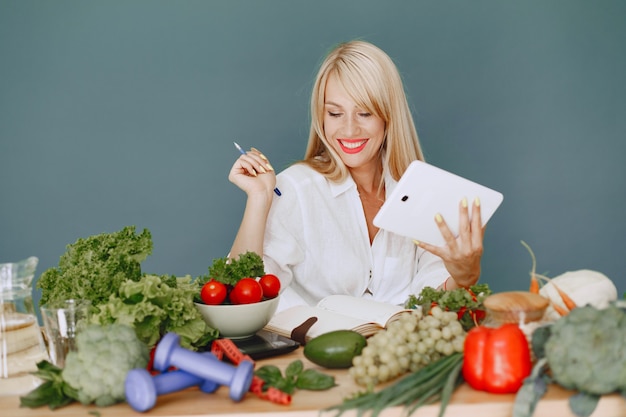 Schönes Mädchen machen einen Salat. Sportliche Blondine in einer Küche. Frau, die Rezept im Notizbuch schreibt.