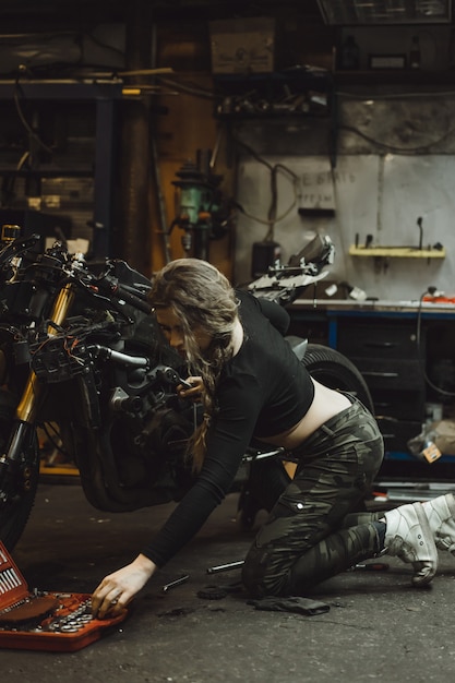 schönes Mädchen mit langen Haaren in der Garage ein Motorrad zu reparieren