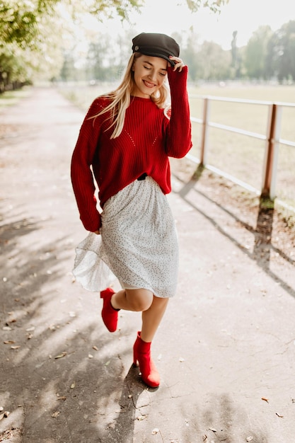 Schönes Mädchen mit trendigen roten Schuhen und weißem Kleid im Wald Charmante Blondine, die sich unter der Sonne auf der Straße glücklich fühlt