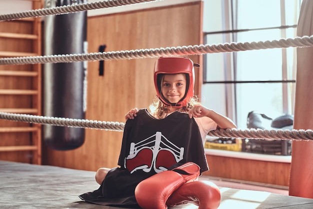 Schönes Mädchen sitzt auf Boxring und trägt Boxeruniform - Handschuhe und Helm.