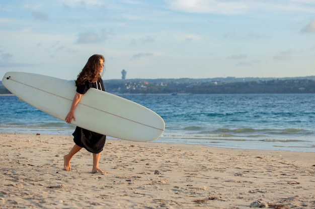 Schönes Mädchen steht am Strand mit einem Surfbrett.
